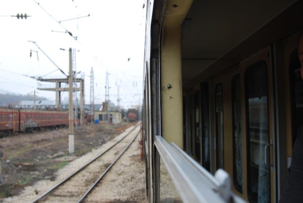 Blick aus einem Zugfenster auf Gleise, Oberleitungen und abgestellte Waggons im Nebel