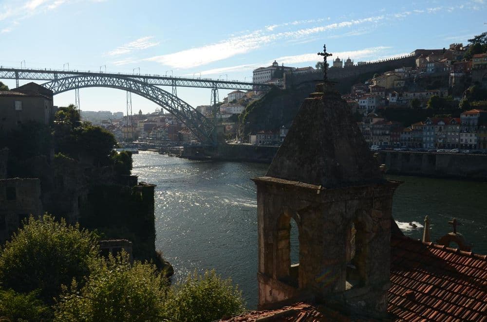 Puente de arco de hierro sobre un río, detrás una ladera con casas de colores