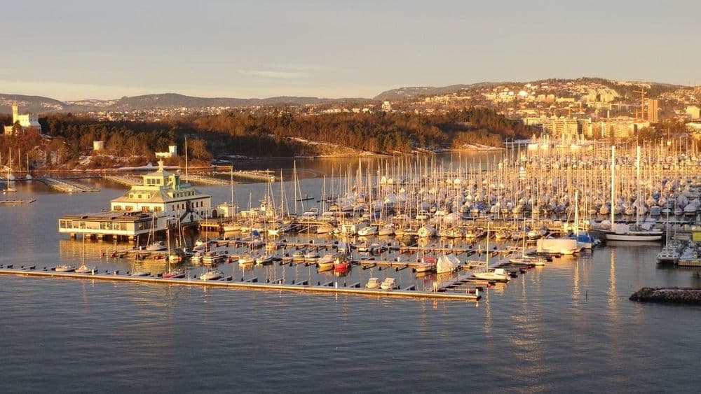 Marina bondée de nombreux voiliers devant une ville vallonnée sous la lumière du soir