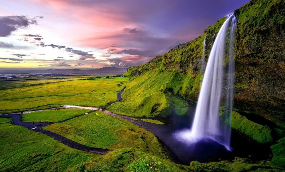 Wasserfall stürzt über eine grüne Klippe in eine weite Ebene bei buntem Abendhimmel